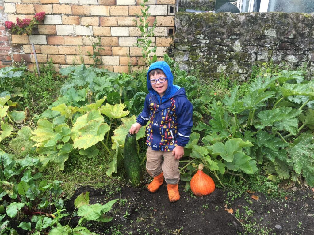 Liam, the inspiration for the garden designers for the Down's Syndrome Scotland Garden is in a pumpkin patch, smiling.