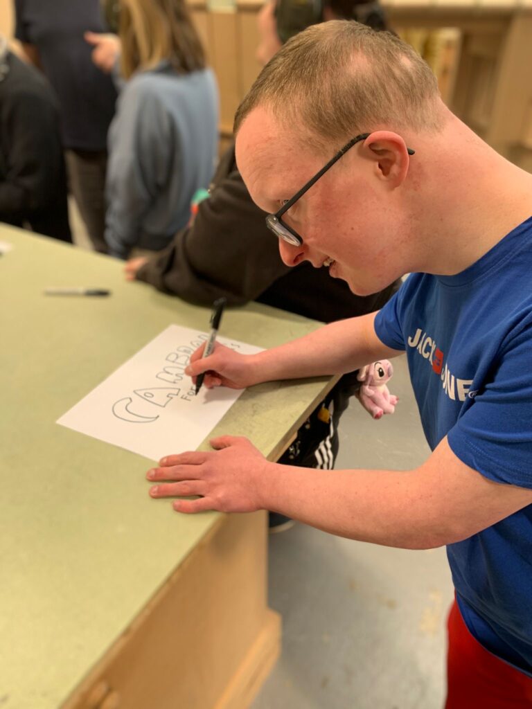 Cameron in a blue t-shirt writing his name to carve